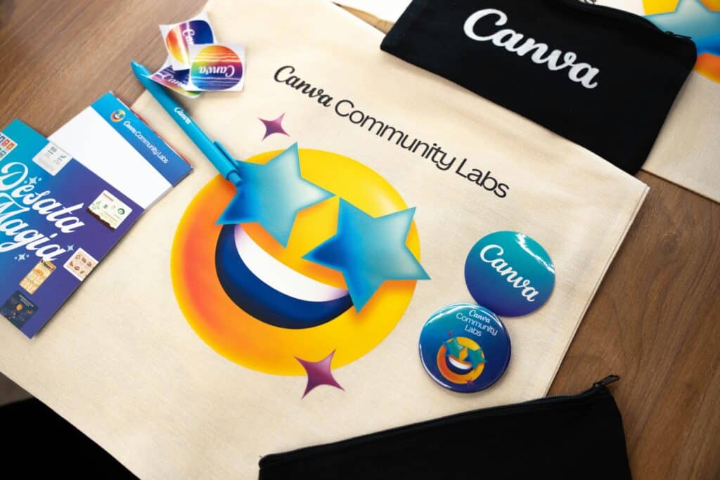 A colorful flat lay of branded company swag, including a Canva tote bag, buttons, stickers, a pen, and a pouch, arranged on a wooden table.