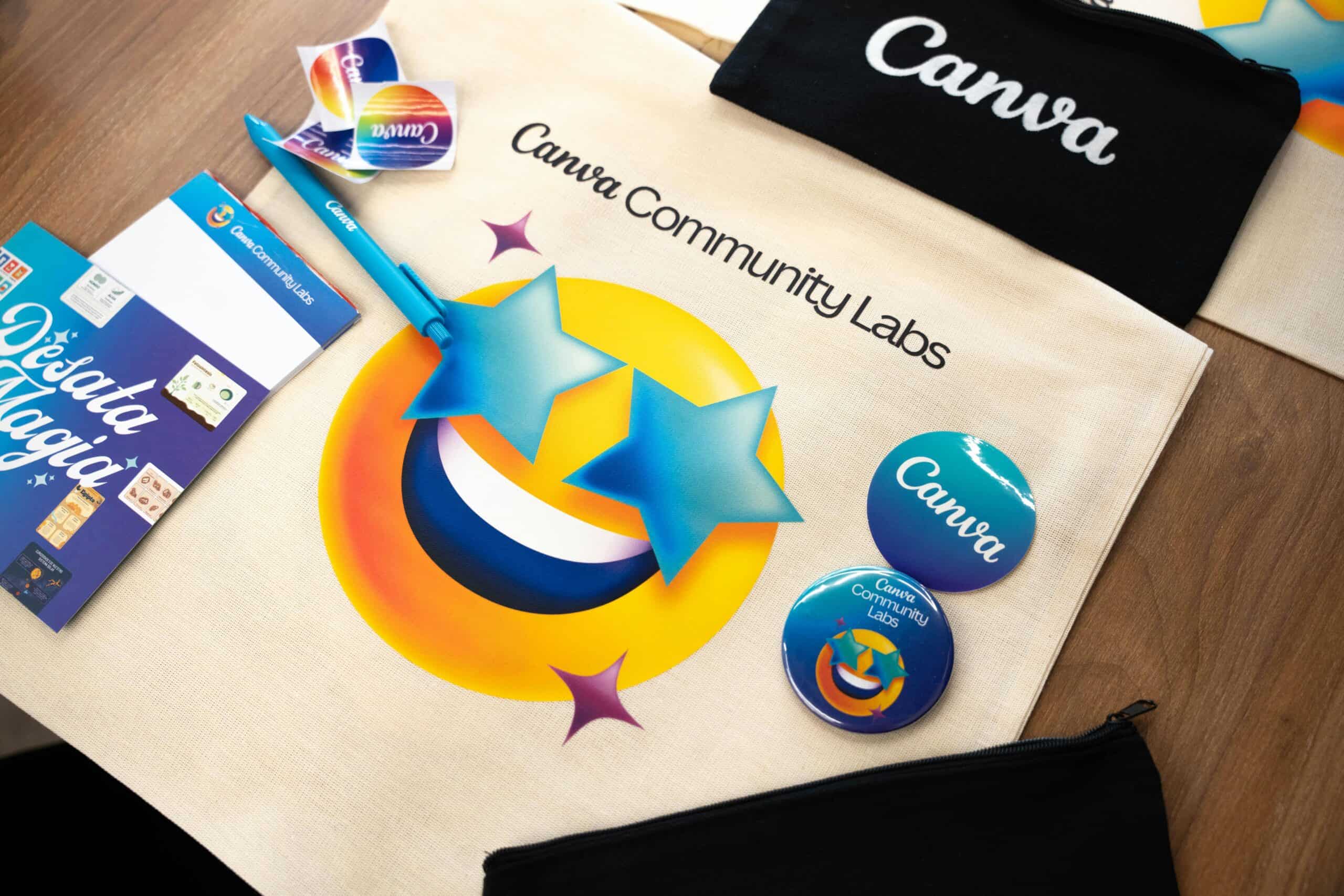 A colorful flat lay of branded company swag, including a Canva tote bag, buttons, stickers, a pen, and a pouch, arranged on a wooden table.