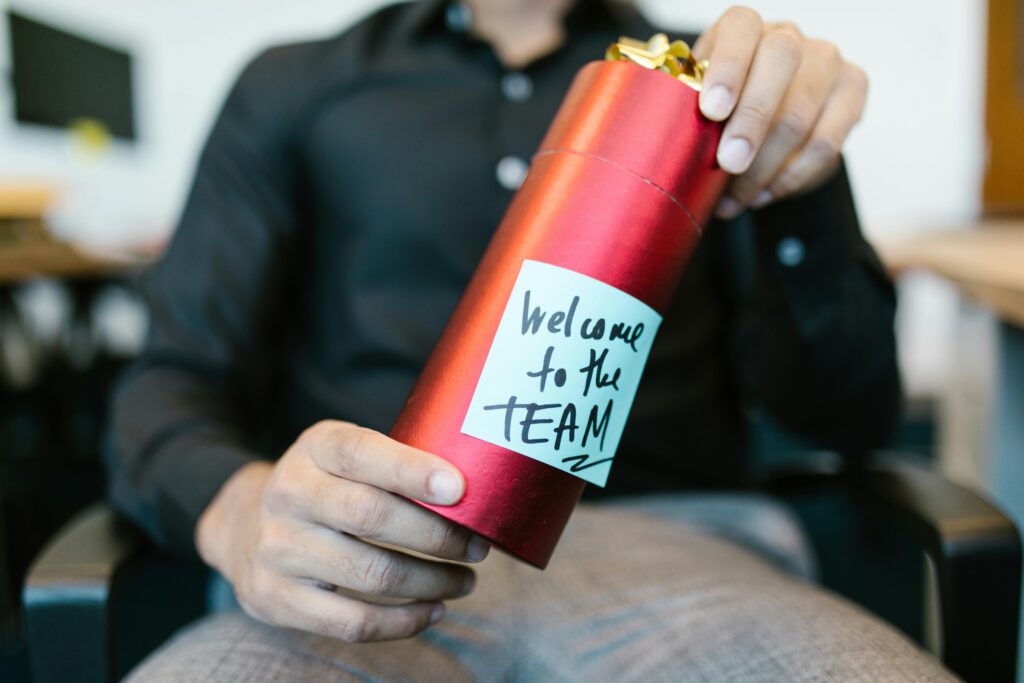 Man holding onboarding kit, packaged in red metallic tube with note that says "welcome to the team."